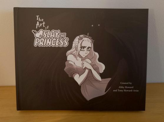 Cover of the Slay the Princess art book. A large, wide format book with white lettering on a textured black background. The title is The Art of Slay the Princess, with credit to Abby Howard and Tony Howard-Arias. The cover artwork depicts the princess, contrasting in bright white against the backdrop, while a tall dark figure with gleaming eyes ominously appears in the background and seems to wrap the princess in large black wings. The art style is stylized, graphic-novel-like with anime leanings, slightly sepia-tinted black and white with sketchy lines and detailed shadows.
